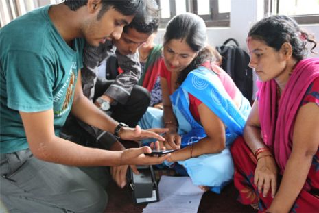 A field worker showing the app on a phone to women seated around a table