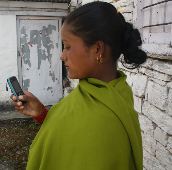A young woman outside a stone house reading content on a feature phone