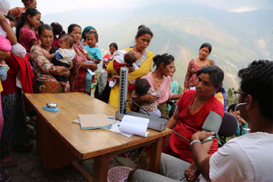 Mothers and infants waiting at an outdoor health check on a Nepali hillside