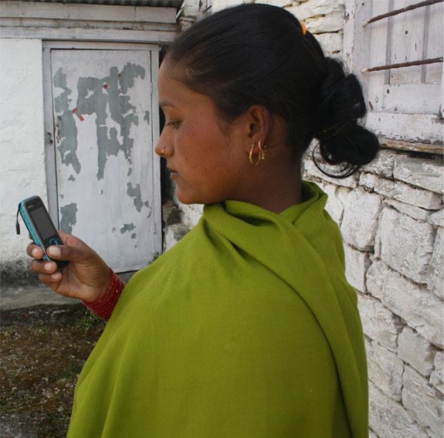 A woman in Nepal using a mobile phone outside her home